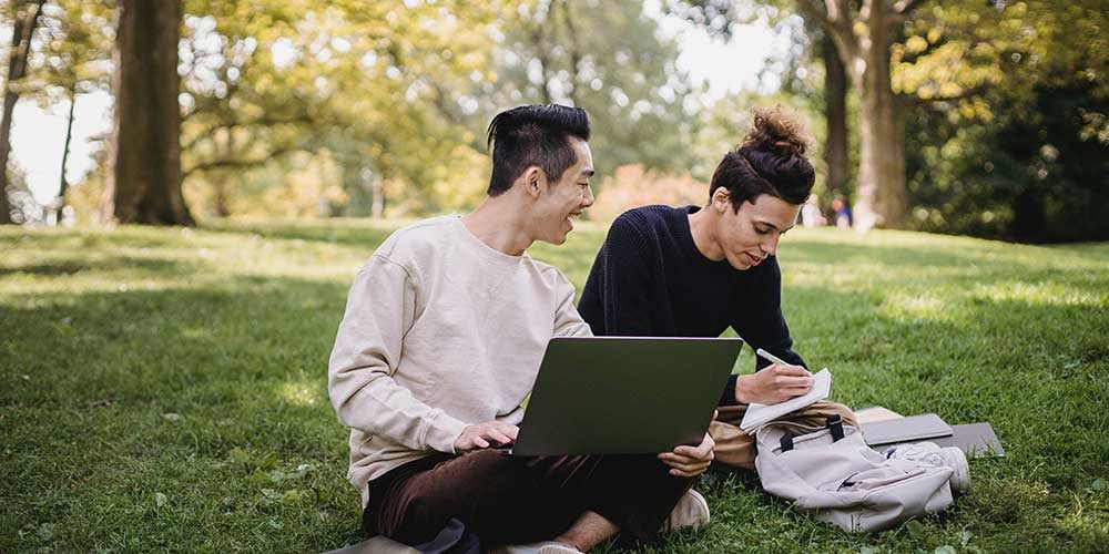 two students studying on a laptop outside