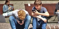 two boys sitting outside looking at their phones