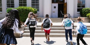 four children with backpacks walking into school 