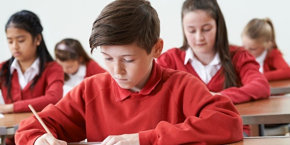 child wearing school uniform taking an exam in an exam hall