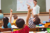 children in primary school classroom raising their hands for the teacher
