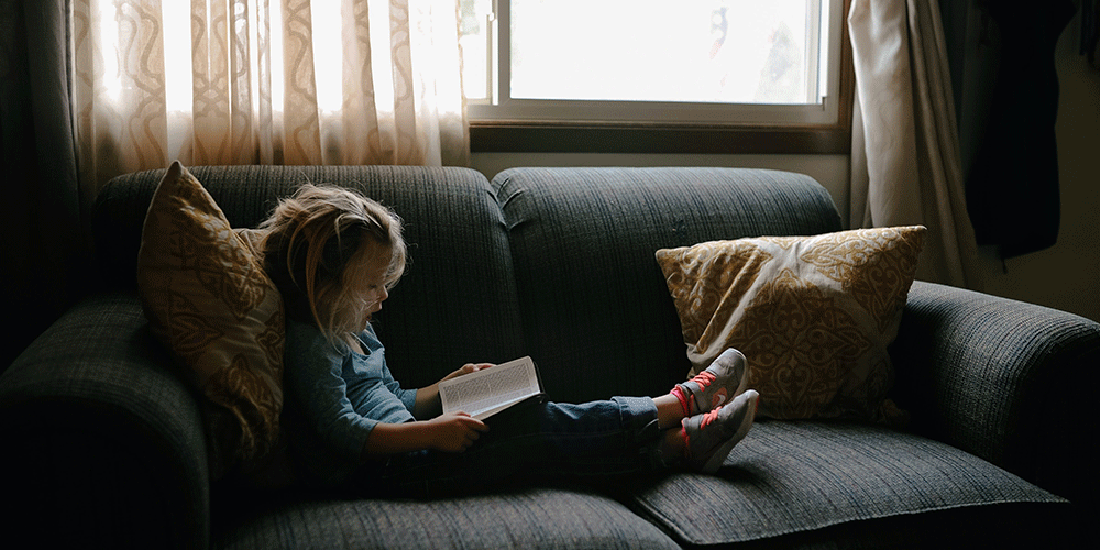 young girl reading aloud on a couch