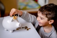 young boy putting money into his piggy bank