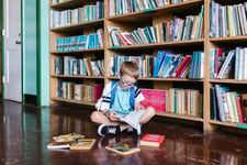 boy sat reading book on floor of library